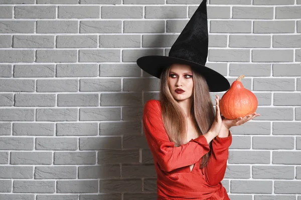 Mulher bonita vestida como bruxa para o Halloween contra a parede de tijolo — Fotografia de Stock