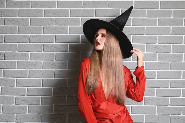 Mulher bonita vestida como bruxa para o Halloween contra a parede de tijolo — Fotografia de Stock