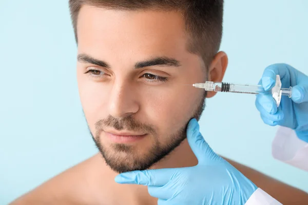Handsome man receiving filler injection on color background — Stock Photo, Image