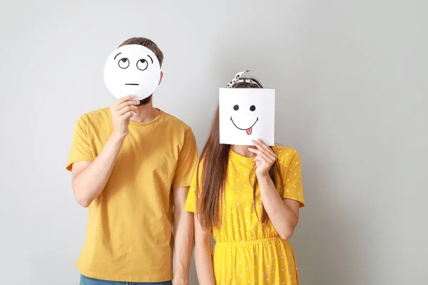 Casal escondendo rostos atrás de folhas de papel com emoticons desenhados em fundo cinza — Fotografia de Stock