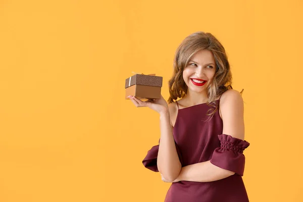 Happy young woman with Christmas gift on color background — Stock Photo, Image