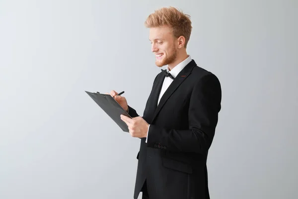 Handsome waiter with clipboard on light background — Stock Photo, Image
