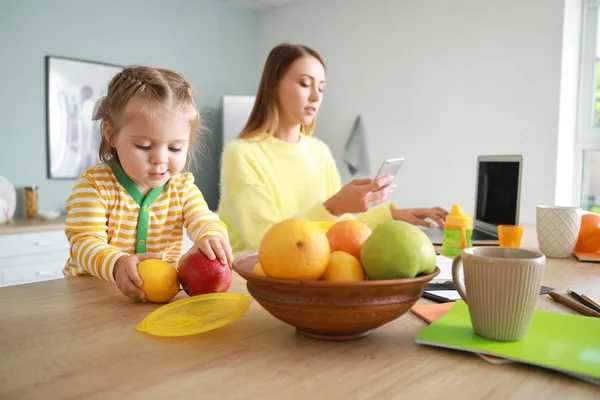 Little daughter with working mother in kitchen at home — Stock Photo, Image