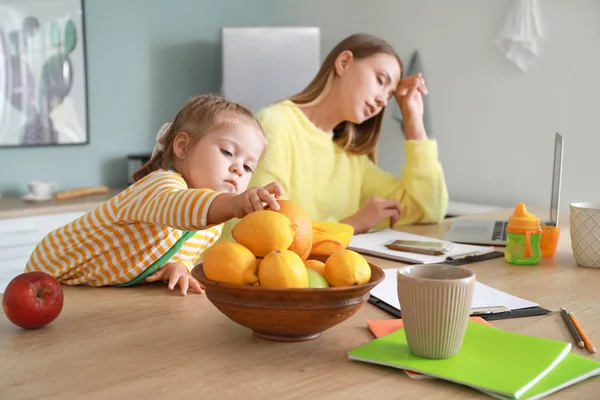 Little daughter with tired mother working in kitchen at home