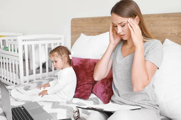 Tired mother with her daughter working in bedroom at home — Stock Photo, Image