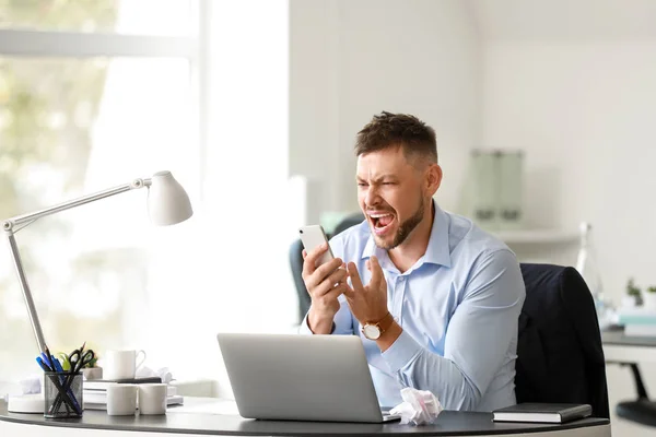 Stressed man talking by mobile phone at table in office — Stock Photo, Image