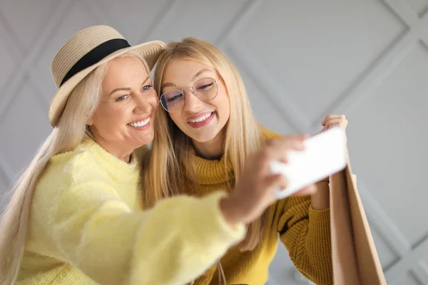 Portrait of happy mother and daughter with shopping bags taking selfie on grey background — Stock Photo, Image