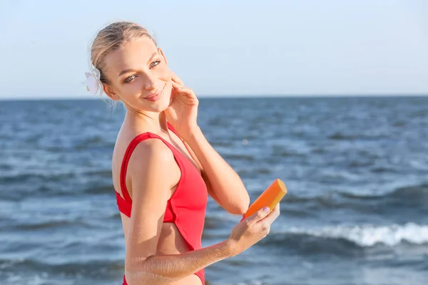 Beautiful young woman with sun protection cream on sea beach — Stock Photo, Image