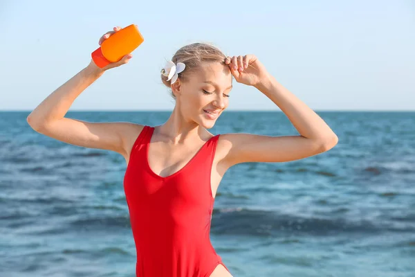 Beautiful young woman with sun protection cream on sea beach — Stock Photo, Image