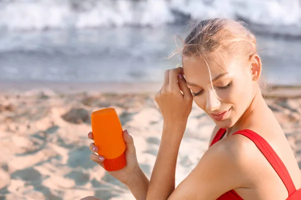 Hermosa mujer joven con crema de protección solar en la playa de mar — Foto de Stock