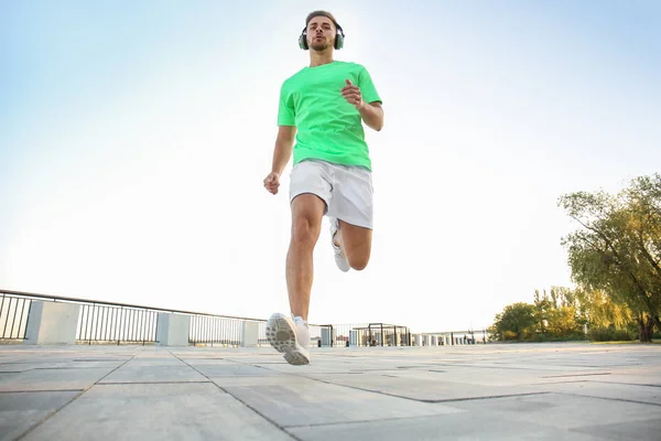 Handsome sporty man listening to music and running outdoors — Stock Photo, Image