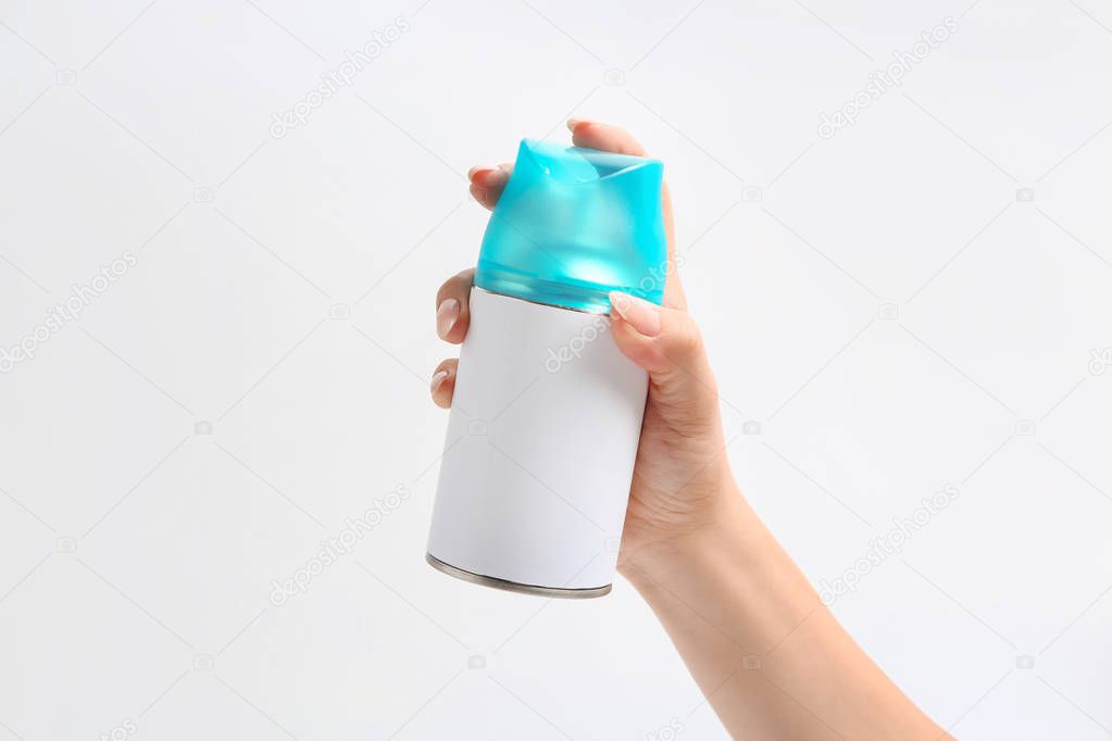 Female hand with bottle of air freshener on light background