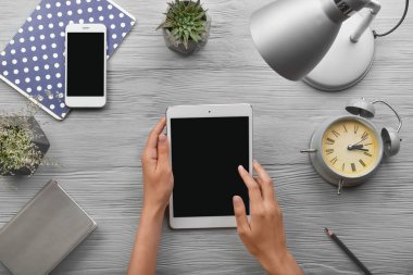 Gri ahşap arka plan üzerinde modern tablet bilgisayar, cep telefonu ve kırtasiye ile Kadın eller