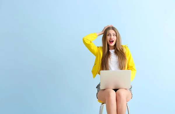 Aufgeregte junge Frau mit Laptop sitzt auf Stuhl vor farbigem Hintergrund — Stockfoto
