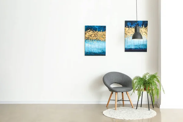 Chair and houseplant near light wall with pictures — Stock Photo, Image