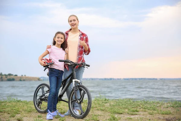 Mulher e sua filhinha com bicicleta perto do rio — Fotografia de Stock