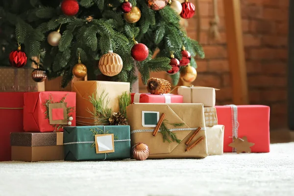Beautiful Christmas gifts under fir tree on floor in room — Stock Photo, Image