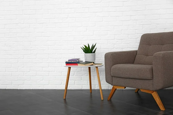 Elegante poltrona con tavolo vicino alla parete di mattoni bianchi in camera — Foto Stock
