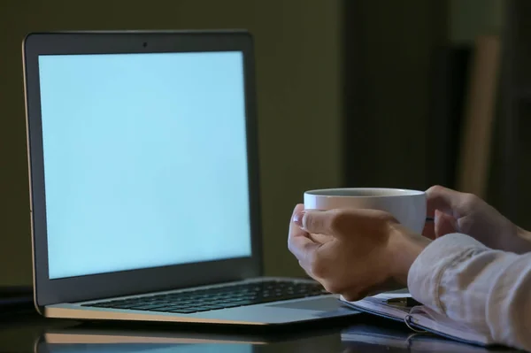 Kvinna med kopp kaffe som arbetar på laptop på kvällen — Stockfoto