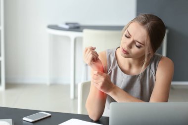 Young woman suffering from pain in wrist at workplace clipart