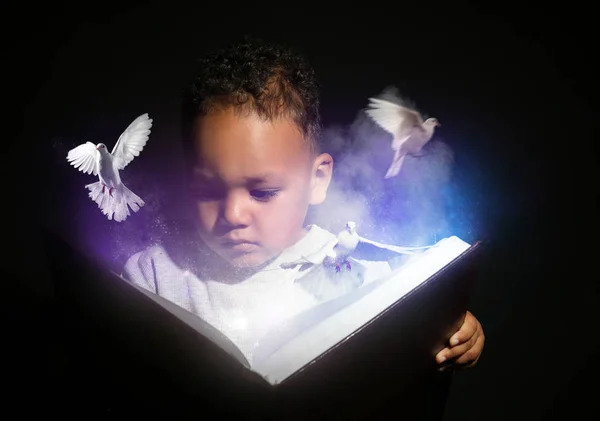 Pequeño niño afroamericano leyendo libro de magia sobre fondo oscuro — Foto de Stock