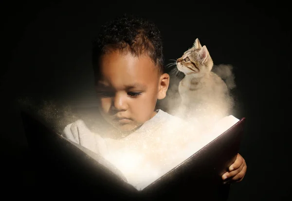 Pequeño niño afroamericano leyendo libro de magia sobre fondo oscuro — Foto de Stock