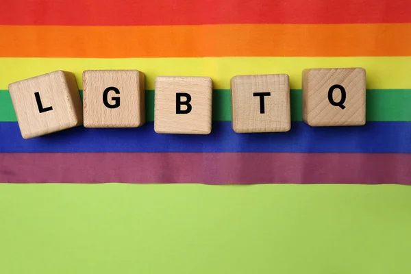 Wooden cubes with abbreviation LGBTQ and rainbow flag on color background — Stock Photo, Image