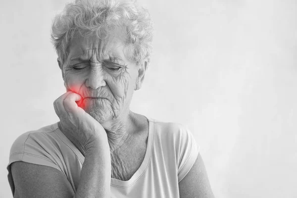 Mulher idosa que sofre de dor de dente no fundo claro — Fotografia de Stock