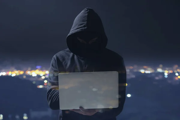 Dupla exposição de hacker profissional com laptop e cidade à noite — Fotografia de Stock