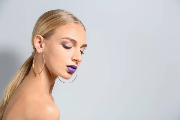 Beautiful young woman with ultra violet lipstick on light background