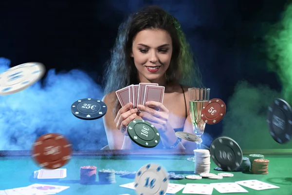 Beautiful female player at table with falling chips in casino — Stock Photo, Image