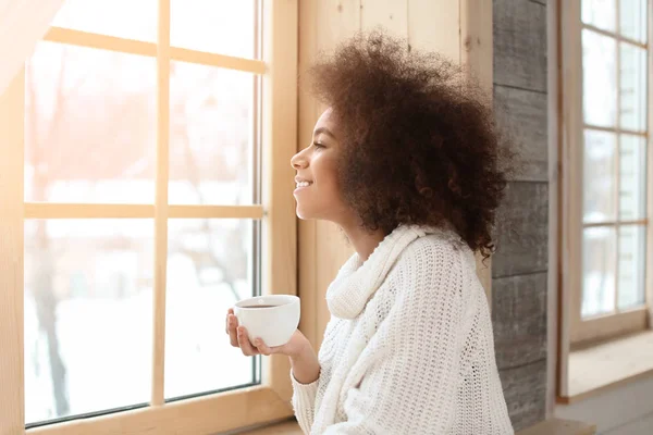 Beautiful African-American woman drinking tea near window — Stock Photo, Image