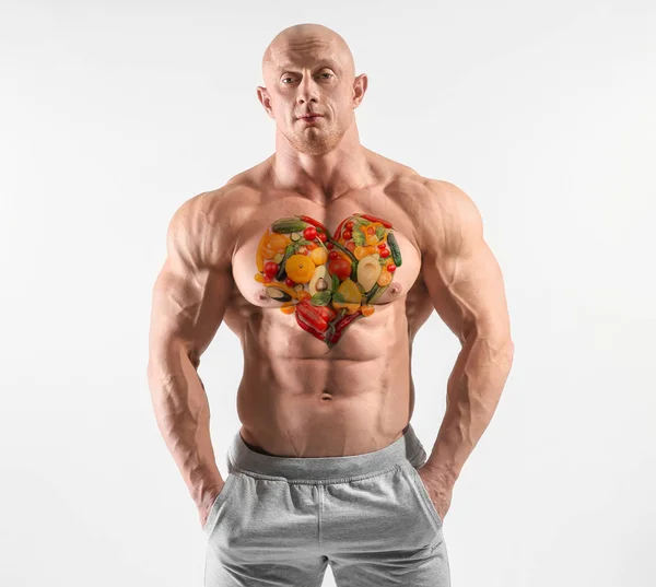 Мышечный культурист с раскрашенными овощами на груди на белом фоне — стоковое фото