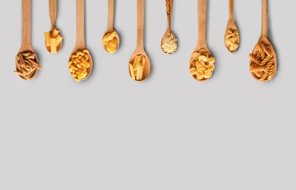 Löffel mit verschiedenen ungekochten Nudeln auf Holzgrund — Stockfoto