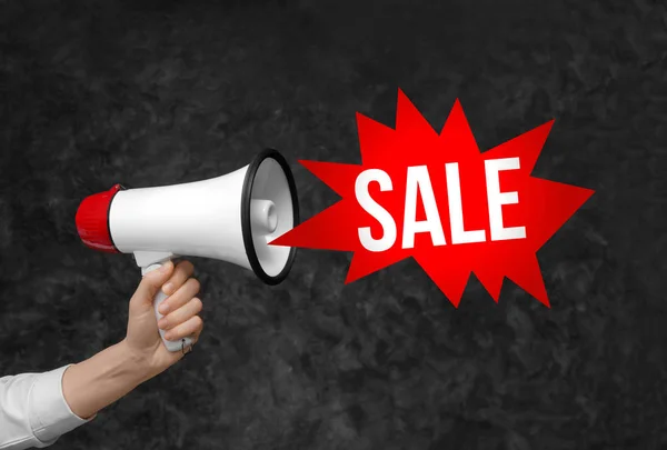 Female hand with megaphone and text SALE on dark background — Stock Photo, Image