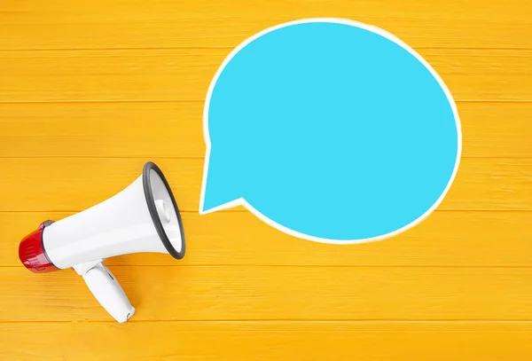 Megaphone and blank speech bubble on color wooden background