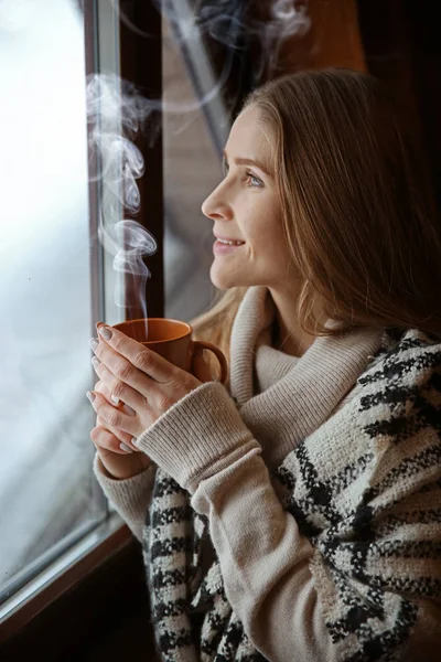 Young woman with hot drink near window on winter day — Stock Photo, Image