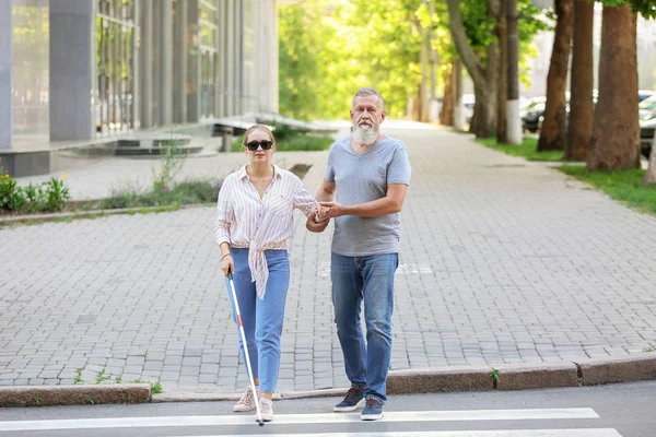 Mature man helping his blind daughter to cross road