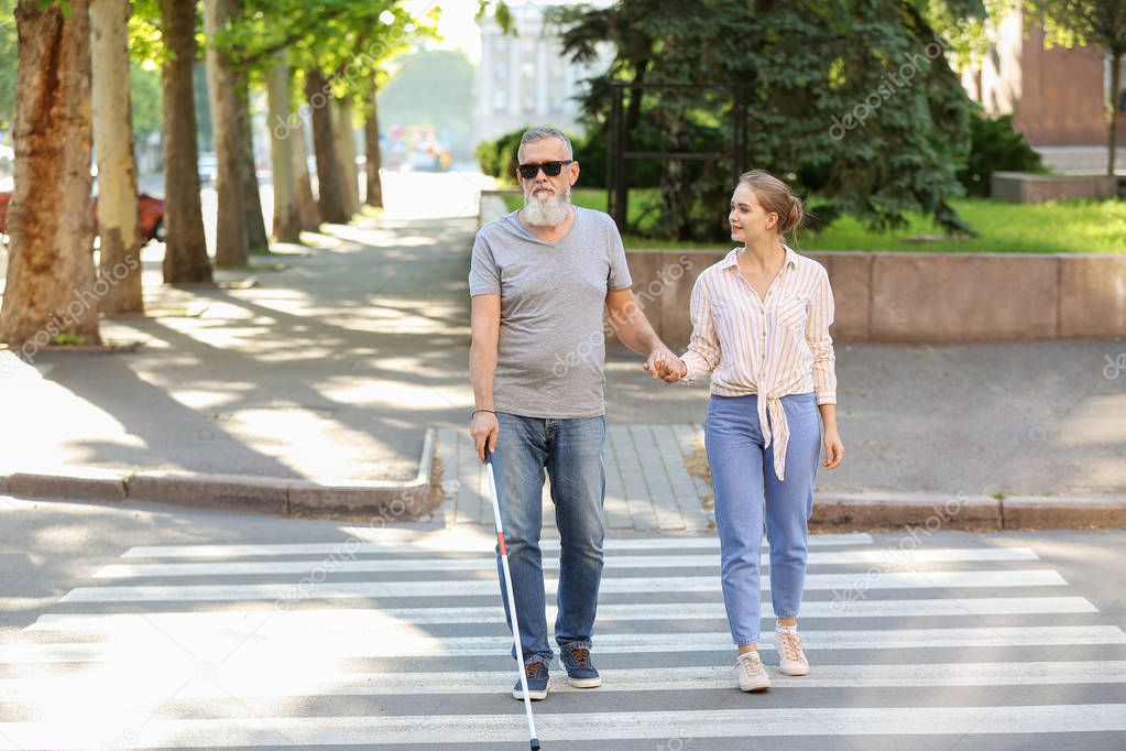 Woman helping blind mature man to cross road