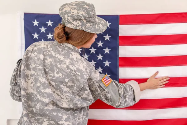 Young female soldier hanging USA flag on wall in headquarters building — Stock Photo, Image