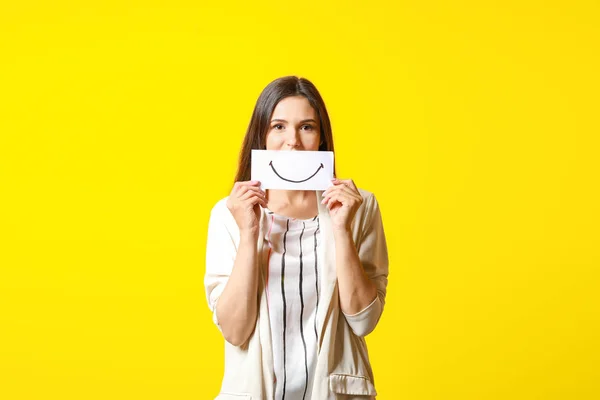 Kvinna gömmer munnen bakom pappersark med ritat leende på färg bakgrund — Stockfoto
