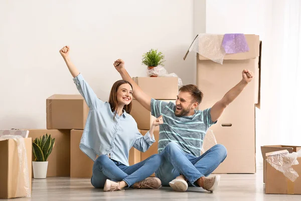Happy young couple with belongings sitting on floor in their new house — Stock Photo, Image
