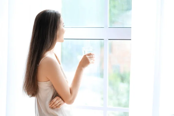 Morning of beautiful young woman with glass of water near window — Stock Photo, Image