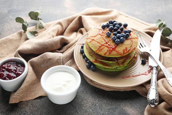 Teller mit grünen Pfannkuchen, Beerenmarmelade und Sauce auf grauem Hintergrund — Stockfoto