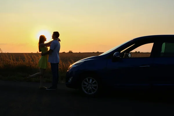 Silueta šťastného páru poblíž svého nového vozu na venkově při západu slunce — Stock fotografie