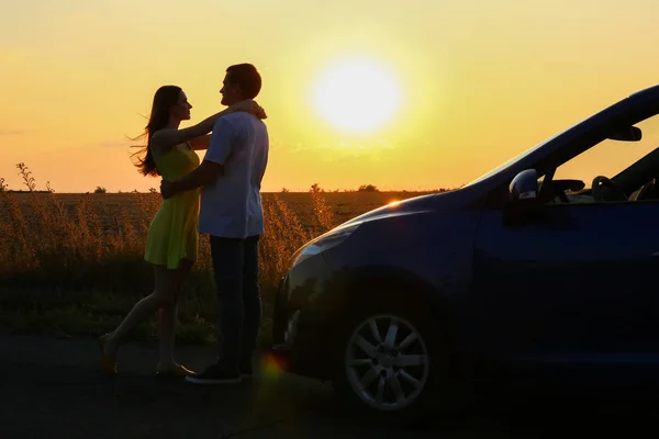 Silhouette de couple heureux près de leur nouvelle voiture à la campagne au coucher du soleil — Photo