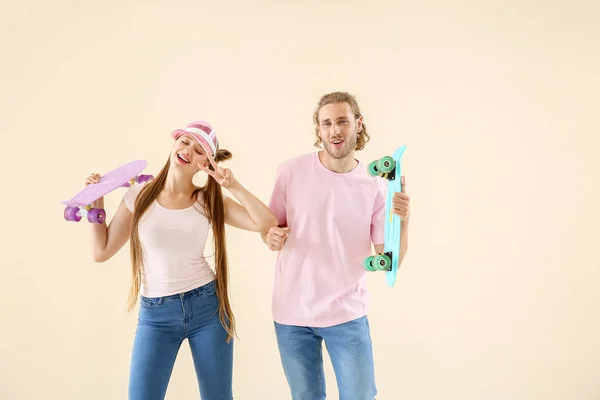 Cool young couple with skateboards dancing against light background — Stock Photo, Image