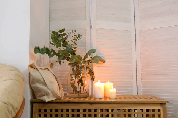 Eucalyptus branches in jar with bag and burning candles on chest in room — Stock Photo, Image