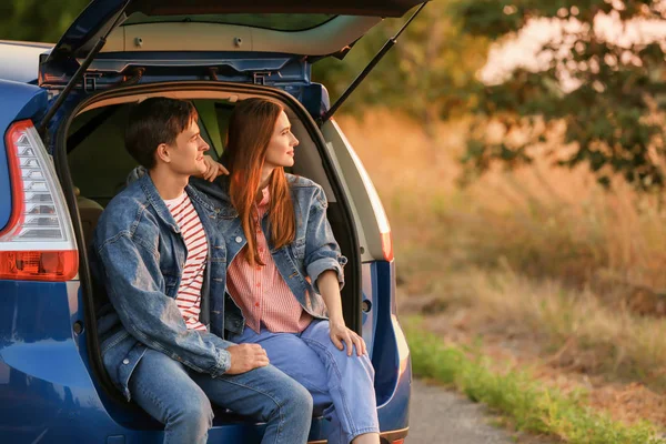 Happy couple sitting in trunk of their new car in countryside — Stock Photo, Image