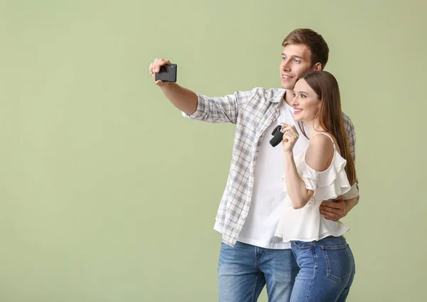 Feliz joven pareja tomando selfie con llave de coche nuevo en el fondo de color — Foto de Stock